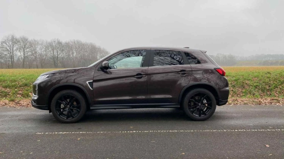 Schwarzer Jeep Kompakt-SUV steht seitlich auf Parkplatz vor grüner Wiese und kahlen Bäumen