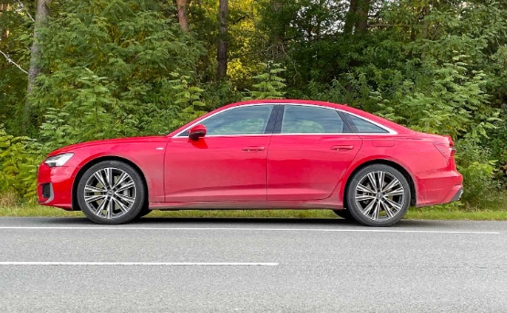 Roter Audi A6 Sedan parkt am Straßenrand vor grünem Waldgebiet mit Bäumen