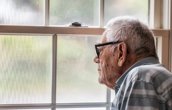 Senior mit Brille blickt suchend aus dem Fenster