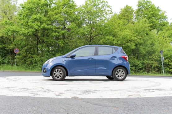 Blauer Kleinwagen steht auf grauem Parkplatz vor grünem Wald und Bäumen