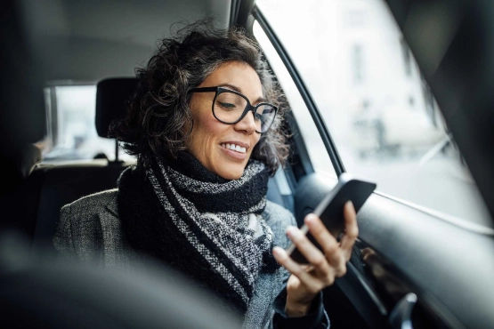 Frau schaut im Auto auf ihr Smartphone.