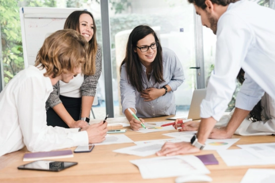 Team im hellen Büro bespricht Designskizzen und Notizen an Holztisch zusammen