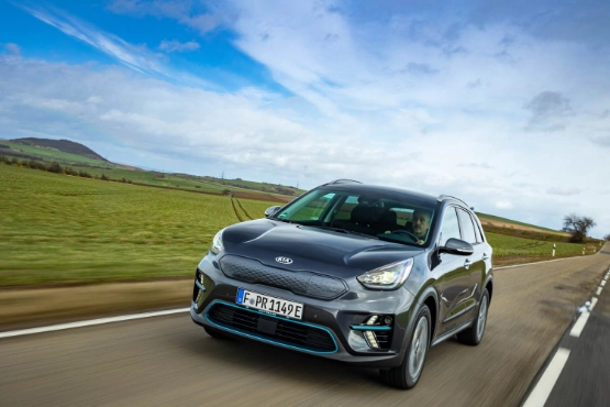 Kia Sportage fährt auf Landstraße durch grüne Hügellandschaft unter blauem Himmel mit Wolken