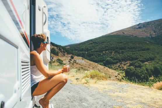 Frau sitzt an Wohnmobil-Tür mit Bergblick, grüne Landschaft und Berghänge im Hintergrund
