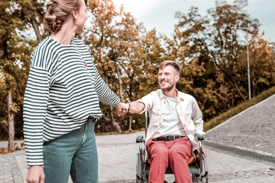 Mann im Rollstuhl der Zeit im Freien mit seiner Freundin verbringt und laechelt waehrend er ihre Hand haelt