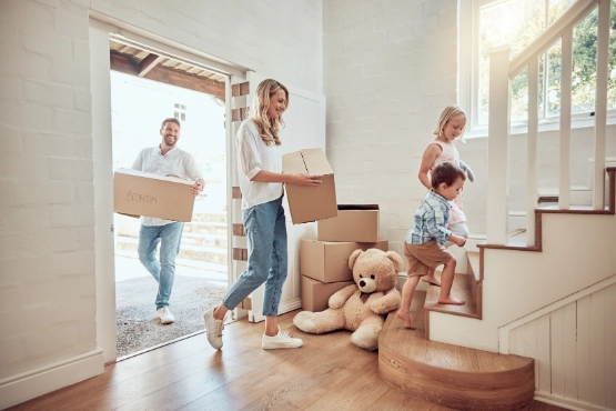 Umzugskosten als Teil der Nebenkosten beim Hauskauf – Paar trägt Umzugskartons in neue Wohnung 