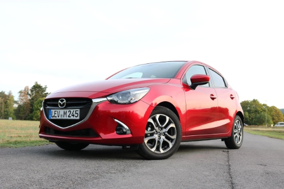 Roter Mazda2 Kleinwagen auf Parkplatz, Seitenansicht mit Blick auf Frontdesign und Räder