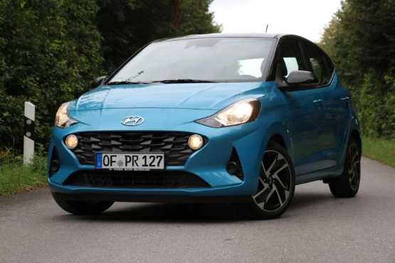Blauer Hyundai i10 mit Kennzeichen auf Landstraße, umgeben von grünen Bäumen