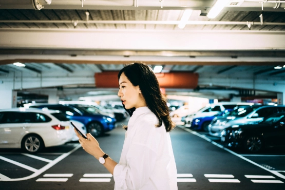 Junge Frau steht in einer Tiefgarage und schaut auf ihr Handy.