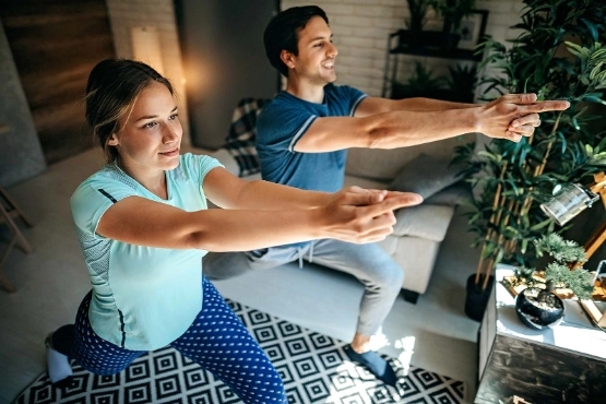 Eine Frau und ein Mann trainieren zuhause auf einer Yogamatte.