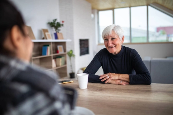 Seniorin und Tochter bei einer Tasse Kaffee zu Hause.