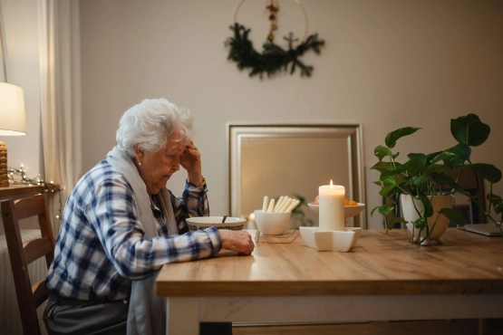 Alte Frau sitzt alleine deprimiert am Esstisch.