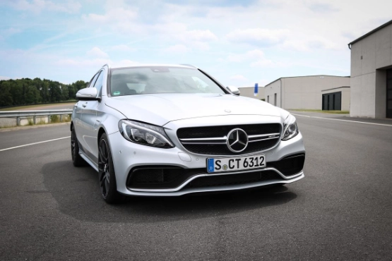 Weißer Mercedes-AMG C63 auf einer Rennstrecke, frontal fotografiert, mit modernem Fabriklager im Hintergrund