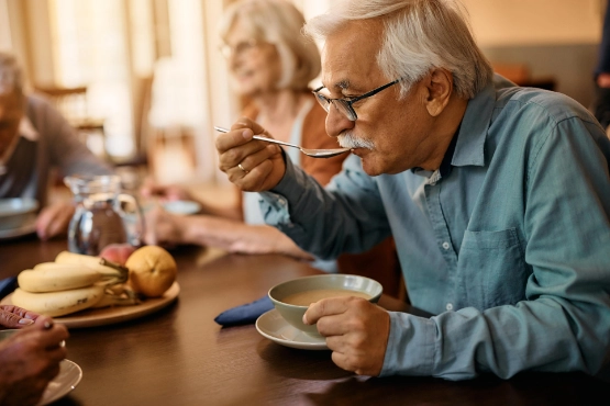 Reifer Mann isst Suppe waehrend er im Pflegeheim den Tag verbringt