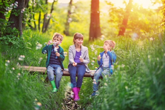 Kinder machen Seifenblasen in der Natur und fühlen sich sicher, weil ihre Eltern an die Kinderabsicherung gedacht haben.
