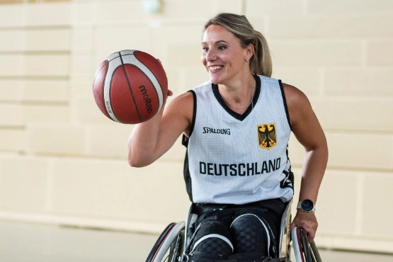 Basketballspielerin in weißem Trikot hält einen roten-weißen Basketball in einer Halle