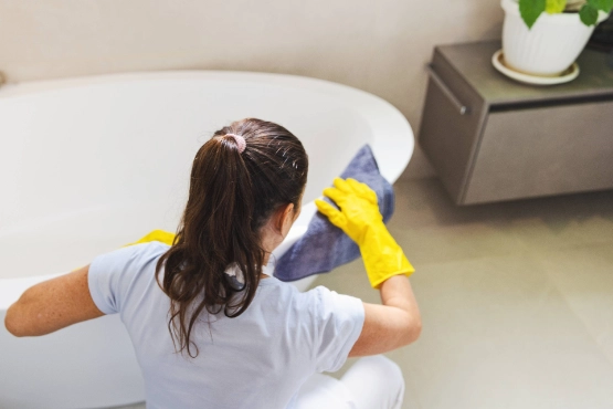 Pflegekraft reinigt Badewanne mit gelben Schutzhandschuhen Hygienemaßnahmen und Sauberkeit in der häuslichen Pflege