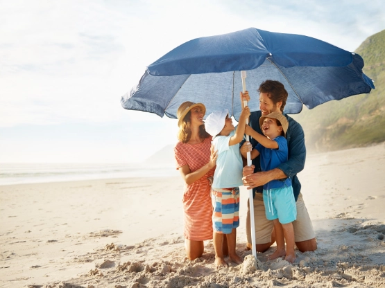 Drei Kinder mit blauem Regenschirm am Strand bei bewölktem Wetter