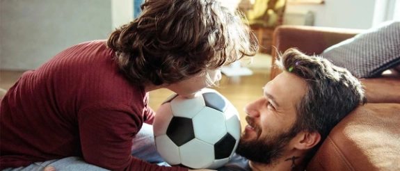 Vater und Sohn spielen mit Fußball auf der Couch im Wohnzimmer