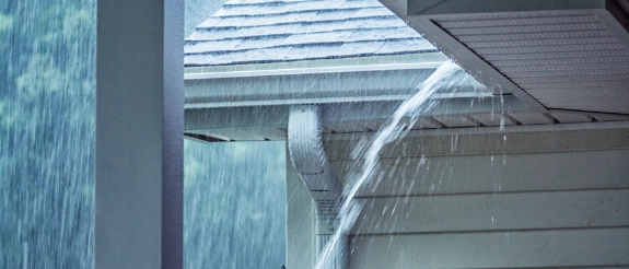 Dachentwässerung mit Wasser, das aus Regenrinne und Fallrohr in starkem Regen läuft