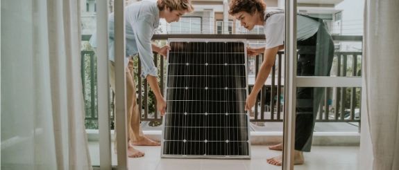 Zwei Personen sitzen auf einem Flur vor einer Glastür, Bücherregale und helles Interieur im Hintergrund