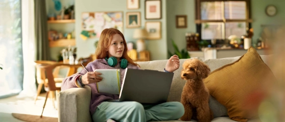 Ein junges Mädchen sitzt auf dem Sofa und erkundigt sich mit ihrem Computer über eine Berufsunfähigkeitsversicherung für Schüler.