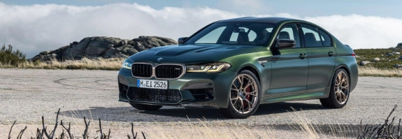 BMW M5 Touring grün-metallic in Küstenlandschaft mit Felsen und Grasland unter blauem Himmel