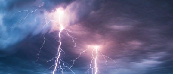 Gewittrige Sturmwolken mit mehreren Blitzentladungen über Baumkronen bei Dämmerung