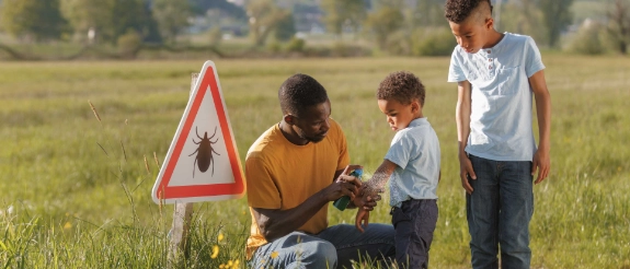 Ein Vater ist meinen Söhnen unterwegs und schützt sie mit Insektenspray vor Zecken.