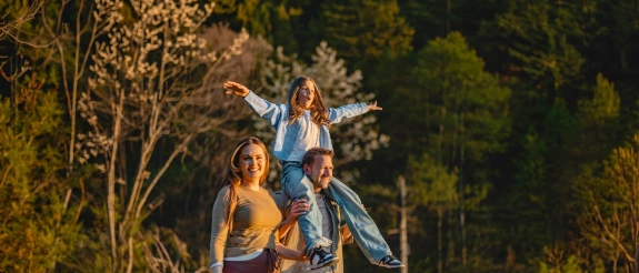 Familie wandert durch den Wald, der Vater trägt die Tochter auf den Schultern.
