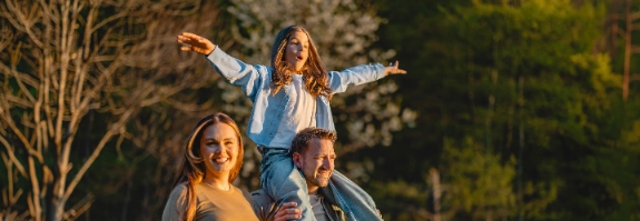 Familie wandert durch den Wald, der Vater trägt die Tochter auf den Schultern.