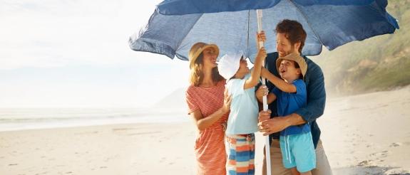 Drei Kinder mit blauem Regenschirm am Strand bei bewölktem Wetter
