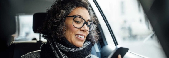 Frau schaut im Auto auf ihr Smartphone.