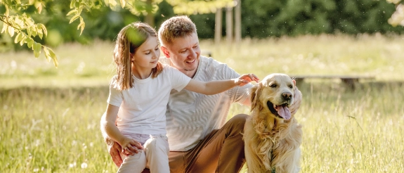 Zwei Kinder streicheln einen großen braunen Hund auf einer grünen Wiese im Freien