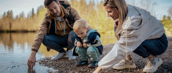 Familie mit Kleinkind spielen am Rande eines Sees mit dem Wasser.