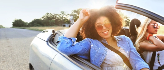 Junge Frauen fahren lachend in offenem Cabrio über sonnige Landstraße, Sommer-Roadtrip