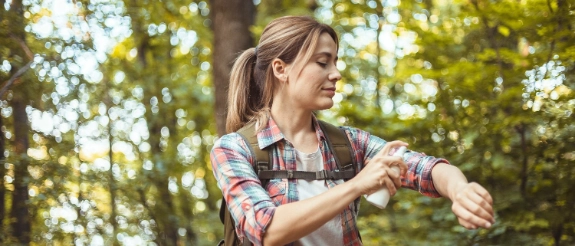 Junge Frau in kariertem Hemd sitzt im Wald und liest in einem Buch, umgeben von grünen Blättern und Bäumen.