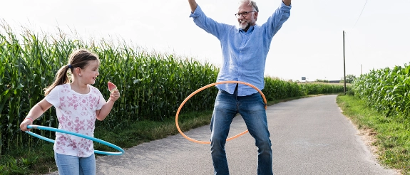 Mädchen spielt mit Hula-Hoop vor Maisfeld, hält Popsicle in der Hand