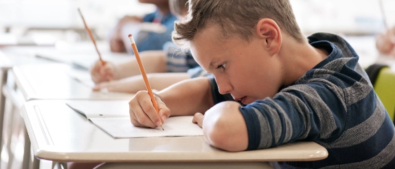 Schüler mit Kopfhörern konzentriert beim Schreiben am Tisch im Klassenzimmer