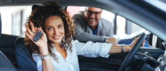 Frau mit Autoschlüssel in der Hand sitzt in ihrem neuen Auto und ist Fahrzeughalter eines Autos.