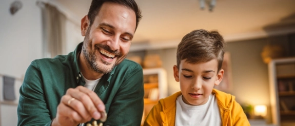 Mit Hilfe der Taschengeldtabelle zählen Vater und Sohn das empfohlene Taschengeld aus einer Spardose.