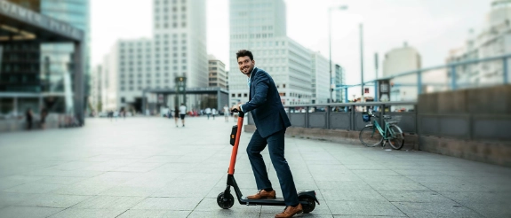 Ein Mann fährt mit seinem E-Tretroller sorglos auf der Straße, weil er eine E-Scooter- Versicherung hat.