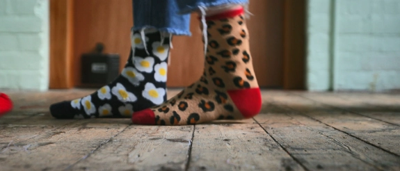 Person mit bunten Socken und Partyhut sitzt auf Holzboden mit Luftschlangen und Konfetti