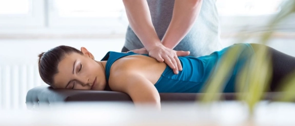 Physiotherapeut behandelt Rücken einer jungen Frau in heller Praxis