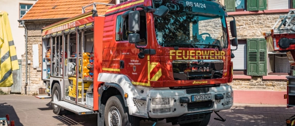 Rotes Feuerwehrfahrzeug MAN mit Leiter parkt vor Fachwerk- und Steingebäuden in deutscher Kleinstadt