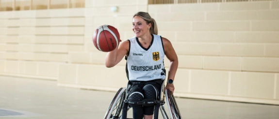 Rollstuhlbasketballerin in deutschem Nationalteam-Trikot hält Basketball in einer Sporthalle