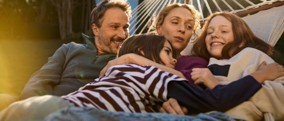 Eine Familie mit Vater, Mutter und zwei Kindern liegt vergnügt in einer Hängematte.