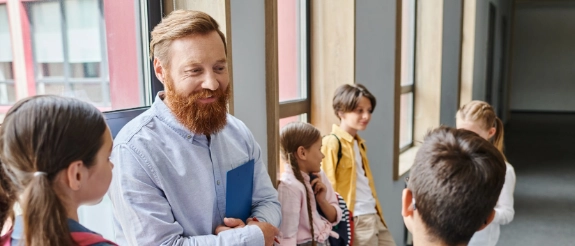 Lehrer unterrichtet Grundschüler im Klassenzimmer, Kinder stehen aufmerksam im Kreis um den Pädagogen herum.