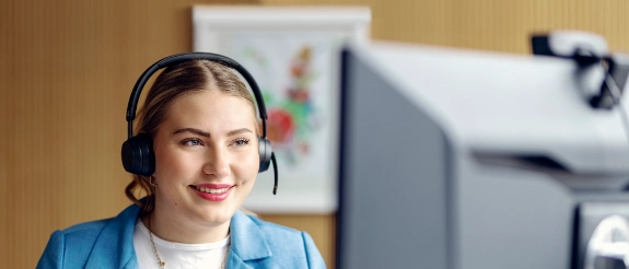 Junge Frau mit Headset vor einem Bildschirm in einer digitalen Beratungssituation.