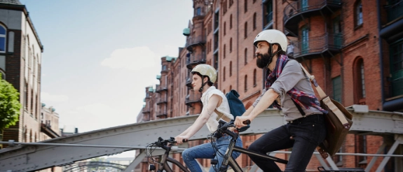 Zwei Personen fahren mit e-bike durch Stadt.